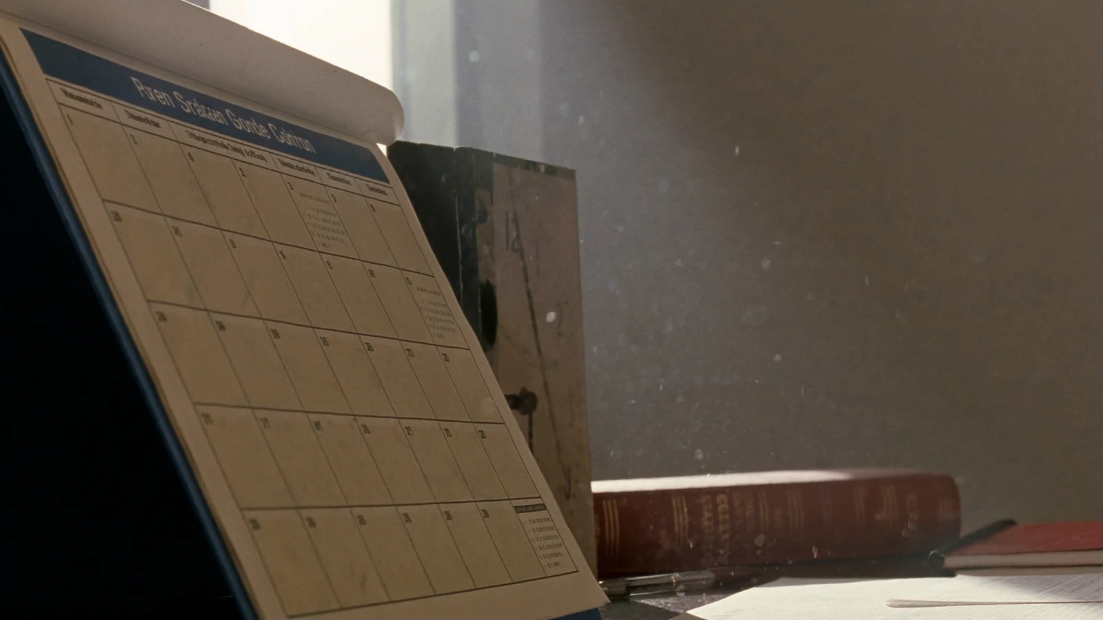 A wall calendar and a statute volume on a desk in raking morning light