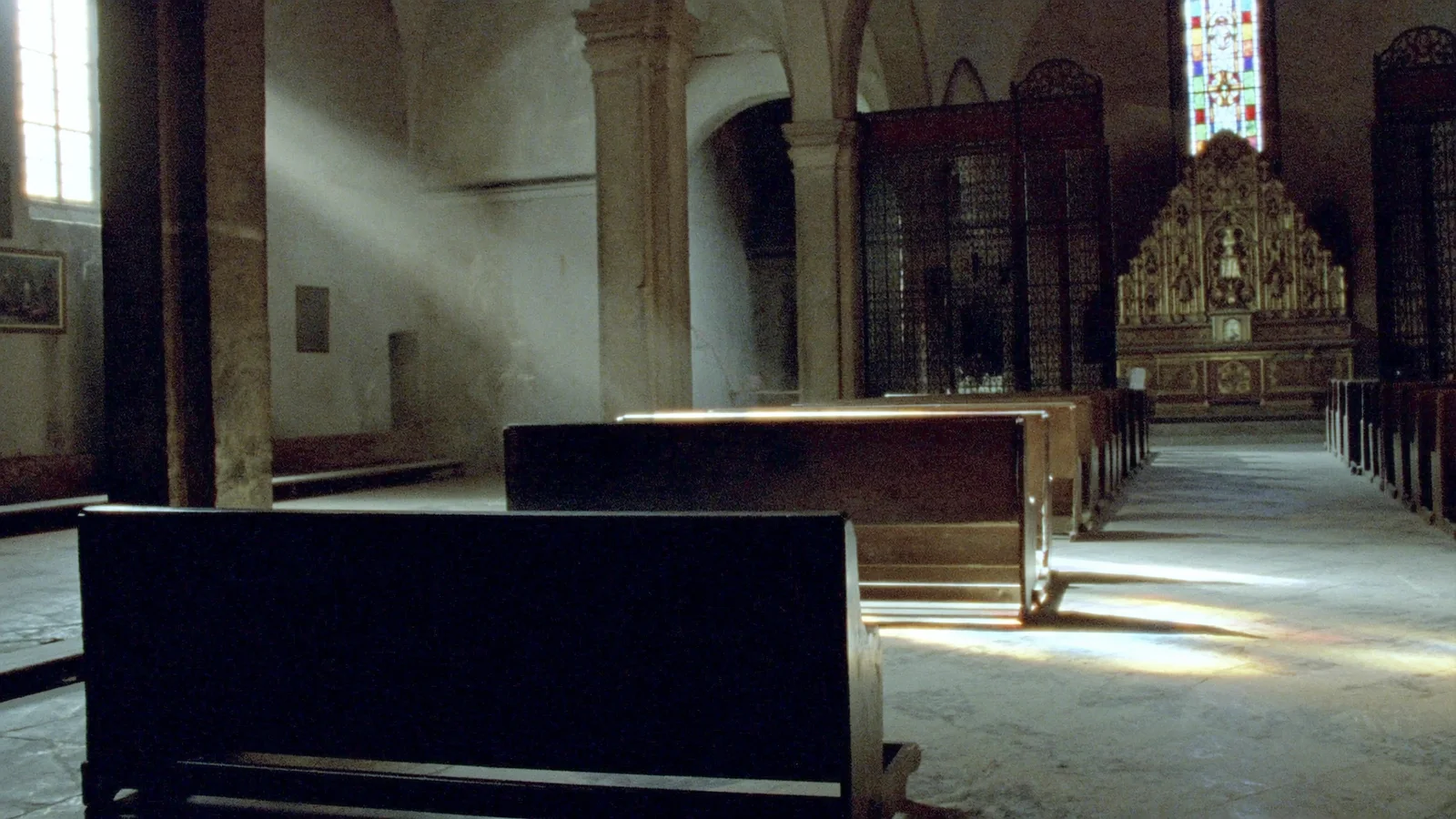 Morning light falling through stained glass across the empty pews of an old Catholic church