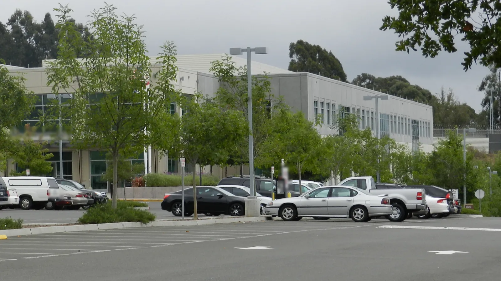 Exterior of the Alameda County Juvenile Justice Center in San Leandro, a two-story pale concrete building behind a parking lot and young trees