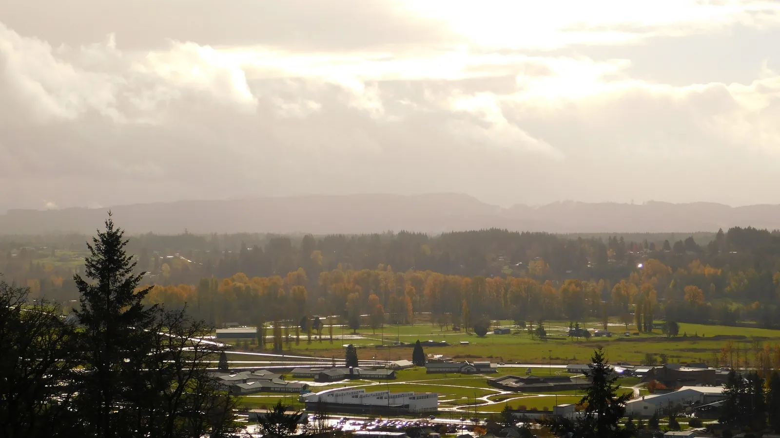 Distant view of the Green Hill School campus in Chehalis, low buildings and playing fields in a river valley with autumn trees and hills behind