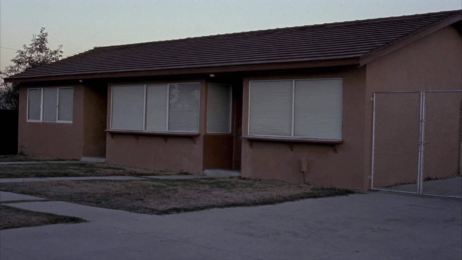A plain single-story group home at dusk with closed blinds and a chain-link side gate
