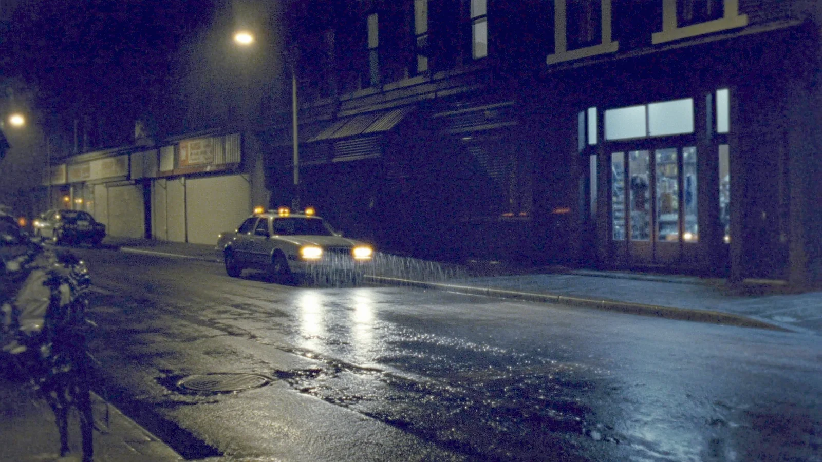 A car idling with hazard lights on a wet, empty city street at night