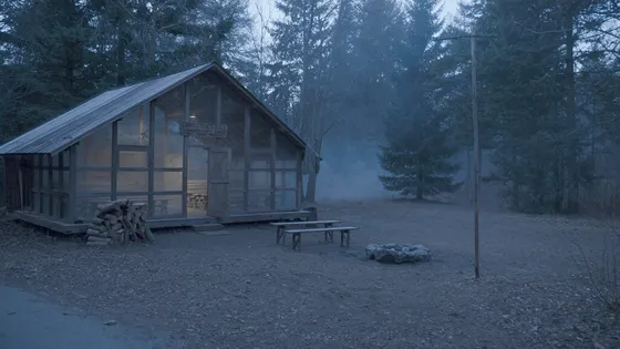 A weathered timber camp lodge in a pine forest at dusk